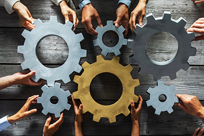 Photo of many pairs of hands holding large cogs that mesh together