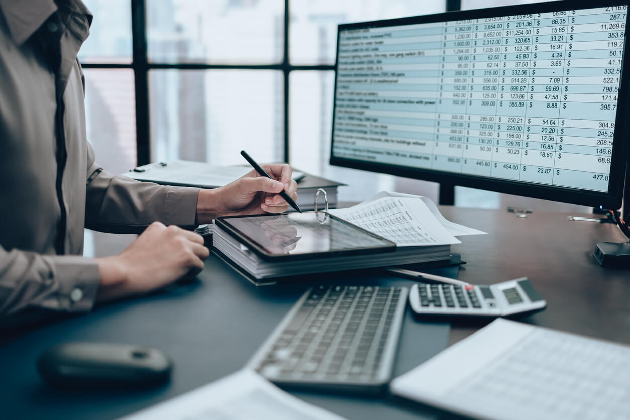 Professional analyzing detailed revenue data on a computer while taking notes in a modern office setting.